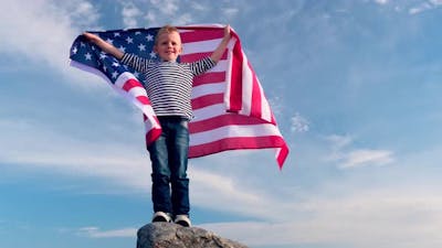 Blonde Boy Waving National USA Flag Outdoors Over Blue Sky at Summer American Flag Country.