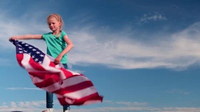 Blonde Girl Waving National USA Flag Outdoors Over Blue Sky at Summer American Flag Country.