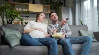 Bored couple at home choose a television show to watch and switch channels with a TV remote control..