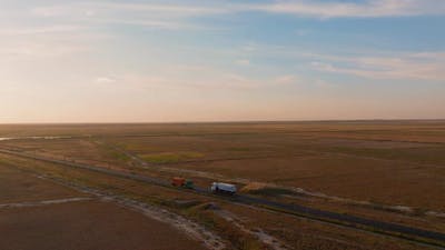 Aerial tracking shot of a transport truck that navigates a straight road, forging ahead towards the .