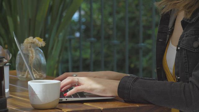 Woman typing on her laptop in a coffee shop .