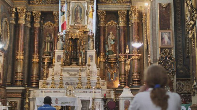 Lady praying in front of a large altar inside a church.