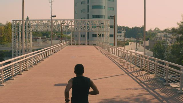 Man jogging on a pedestrian bridge in the city.