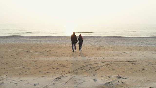 Couple holding hands walking on beach towards sea .