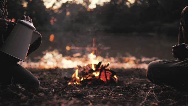 People pouring a warm drink around a campfire.