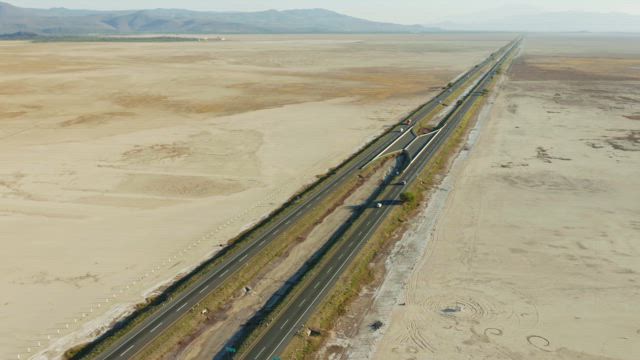 A steady stream of trucks and vehicles traversing the expansive highway in the middle of the arid landscape.