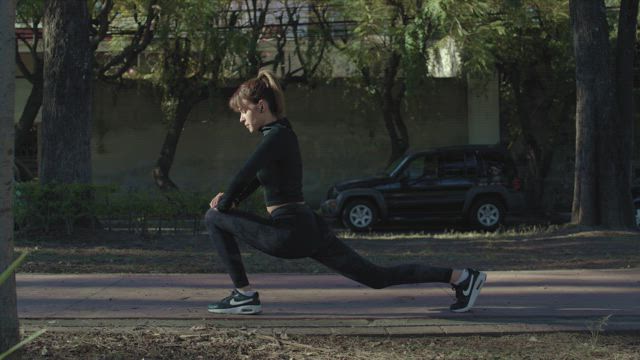 A young runner woman wearing a snugly black attire does long lunges as warm up before her morning run.