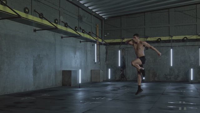 A young shirtless man on his fitness training session doing jumping lunges at the gym.