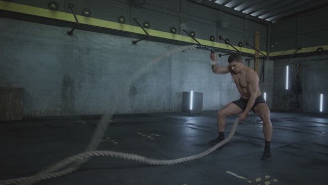 A young man training his muscular physique shaking the battle ropes with strength and determination at the gym.