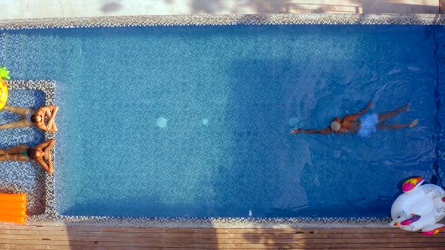 A young man crosses the swimming pool from side to side towards two young girls wearing bikinis.