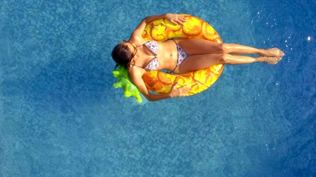 A young woman wearing a bikini enjoys a hot summer day at the pool by sliding on the swimming pool on a vibrant yellow floaty.