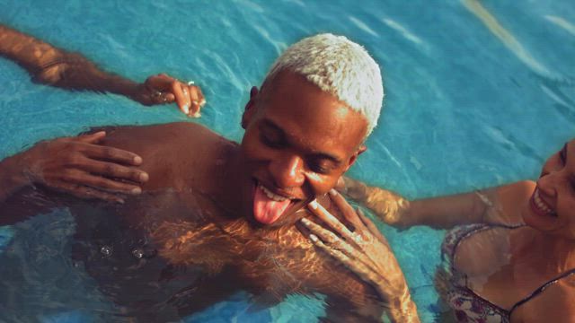 Two young woman push a young black man into the refreshing waters of the swimming pool in slow motion.